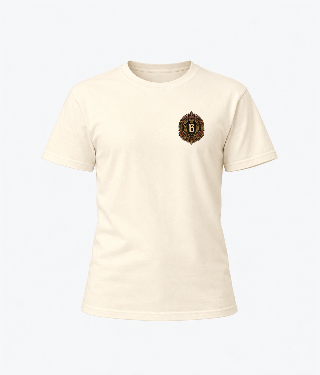 Front product view of the ivory Buchner's Bierhalle Oktoberfest 2026 commemorative T-shirt with a small stylized Buchner's crest on the left chest.