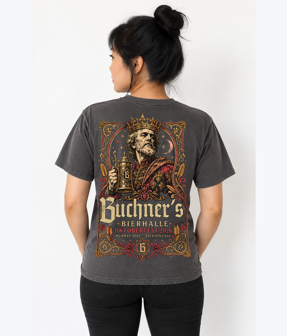 A woman shown from the back wearing a dark gray graphic t-shirt with a large vintage-style print of a crowned man holding a beer stein and the text 'Buchner's Bierhalle Oktoberfest 2023'.