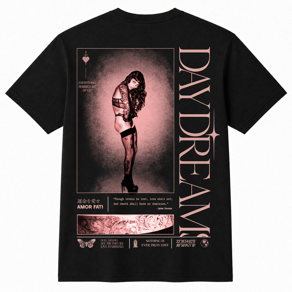 A black short-sleeve t-shirt shown from the back, featuring a large graphic print with a woman in a pink-toned portrait, vertical text reading 'DAYDREAM', and smaller decorative text and illustration elements.