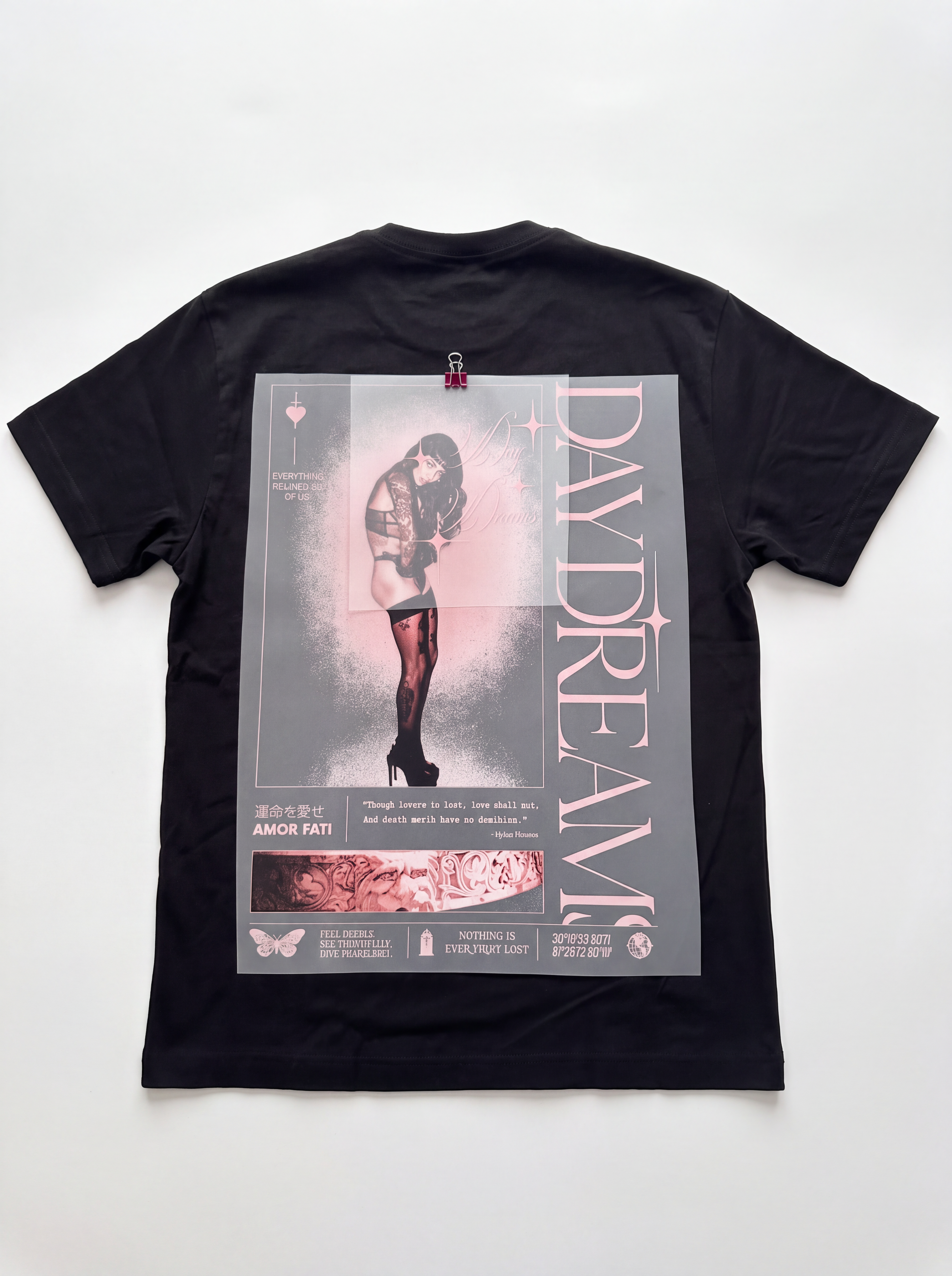A black short-sleeve t-shirt laid flat on a white background, featuring a large graphic print on the back with a pink-tinted illustration of a woman, the text 'DAYDREAM' in vertical pink letters, and smaller graphic elements.